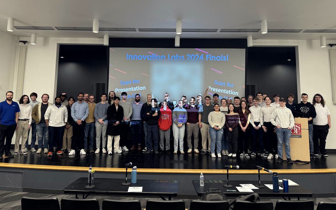 The Innovation Labs 2024 teams on stage at the finals, with the judges' tables in front.