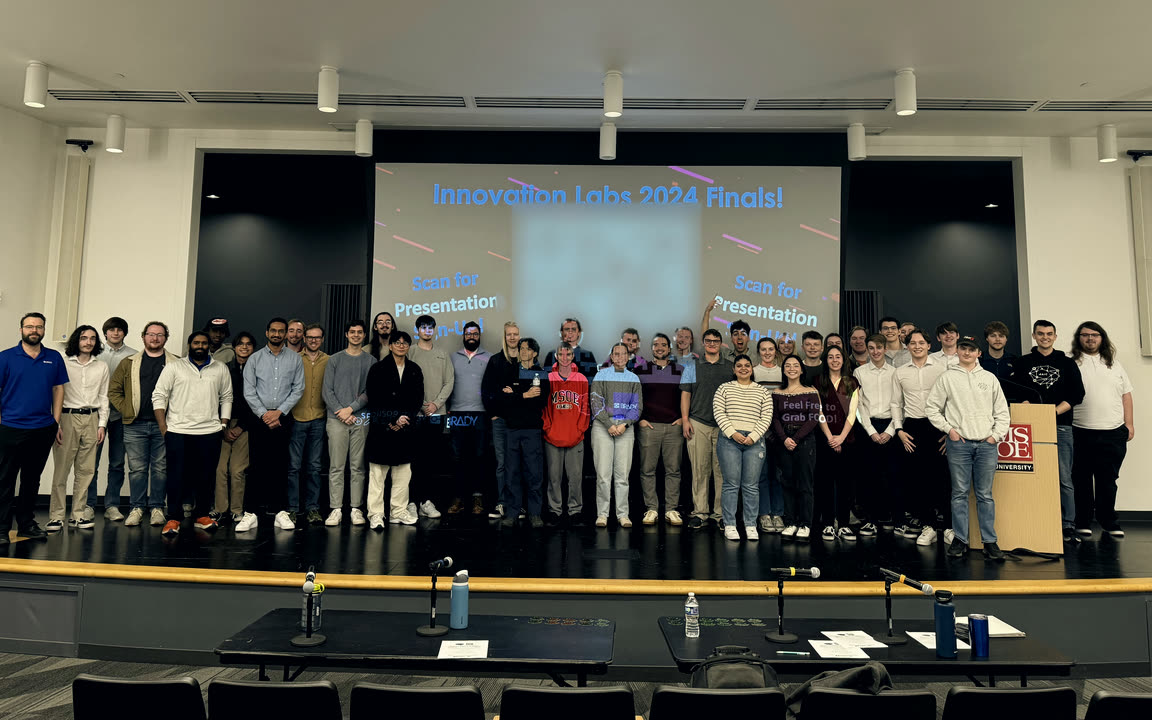 The Innovation Labs 2024 teams on stage at the finals, with the judges' tables in front.
