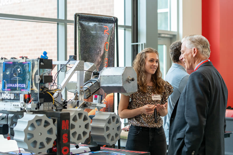 A student shows a robot to a guest at a demo of student AI projects.