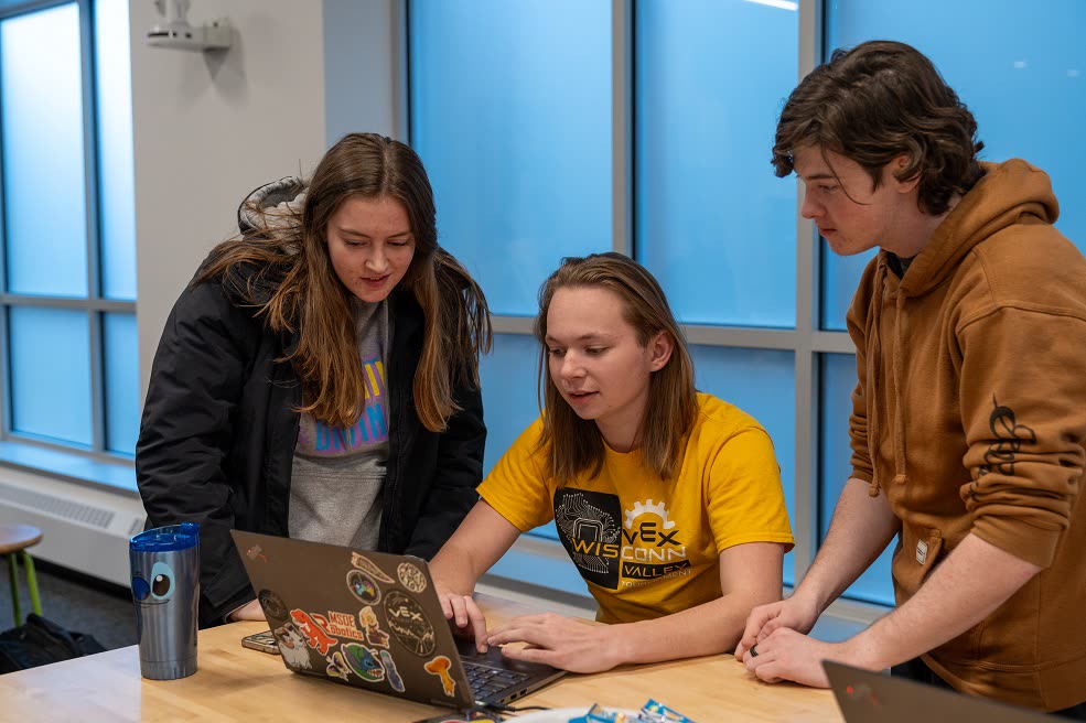 Three students work at a laptop at our first hackathon, in 2023.
