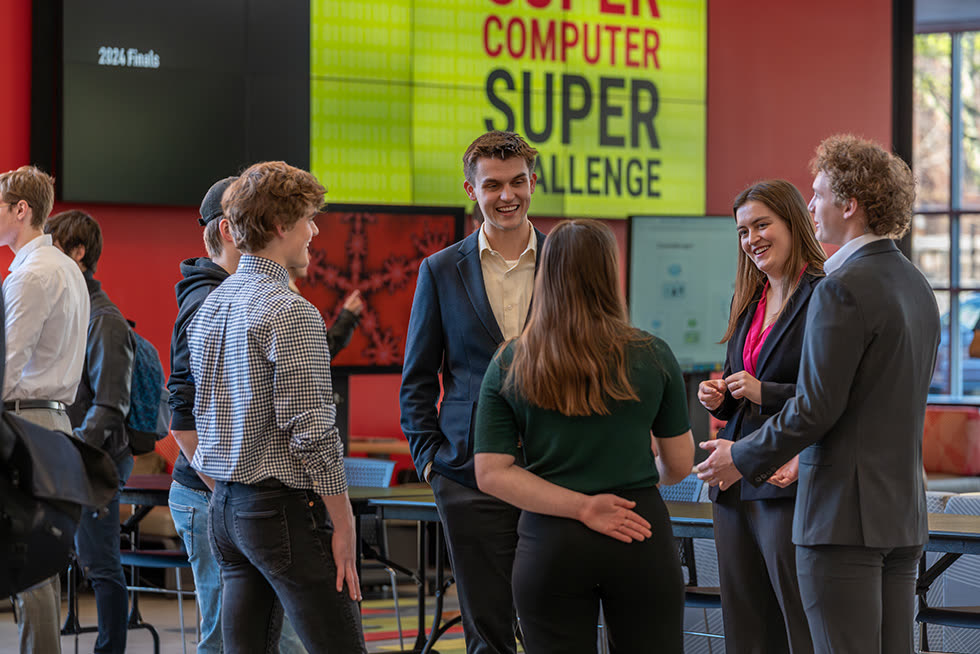 Students and industry guests talk under the Supercomputer Super Challenge banner.